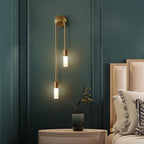 The Clérachic gold stick sconce mounted beside a bed in a teal-panelled room, both shades lit warm.