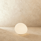 Clérachic frosted white glass goose-egg light glowing warm on a stone ledge in front of a textured plaster wall.