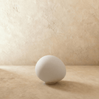 Clérachic frosted white glass goose-egg light switched off, resting on its small white base against a plaster wall.