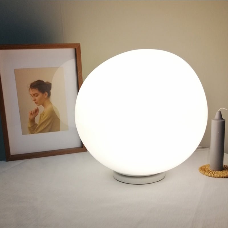 Clérachic large glowing opal glass globe light on a round base, standing on a white tabletop beside a framed portrait and candle.