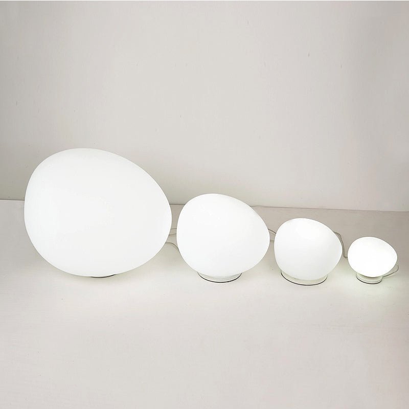 Clérachic row of four lit opal glass egg lights from large to small, standing on a pale surface against a plain wall.
