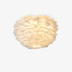 White goose-feather ceiling light from Clérachic glowing warm, with layered feathers forming a rounded shade, on a plain white backdrop.