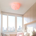 Pink feather ceiling light from Clérachic above a bright room with three tall windows, built-in cupboards and a pink window seat.