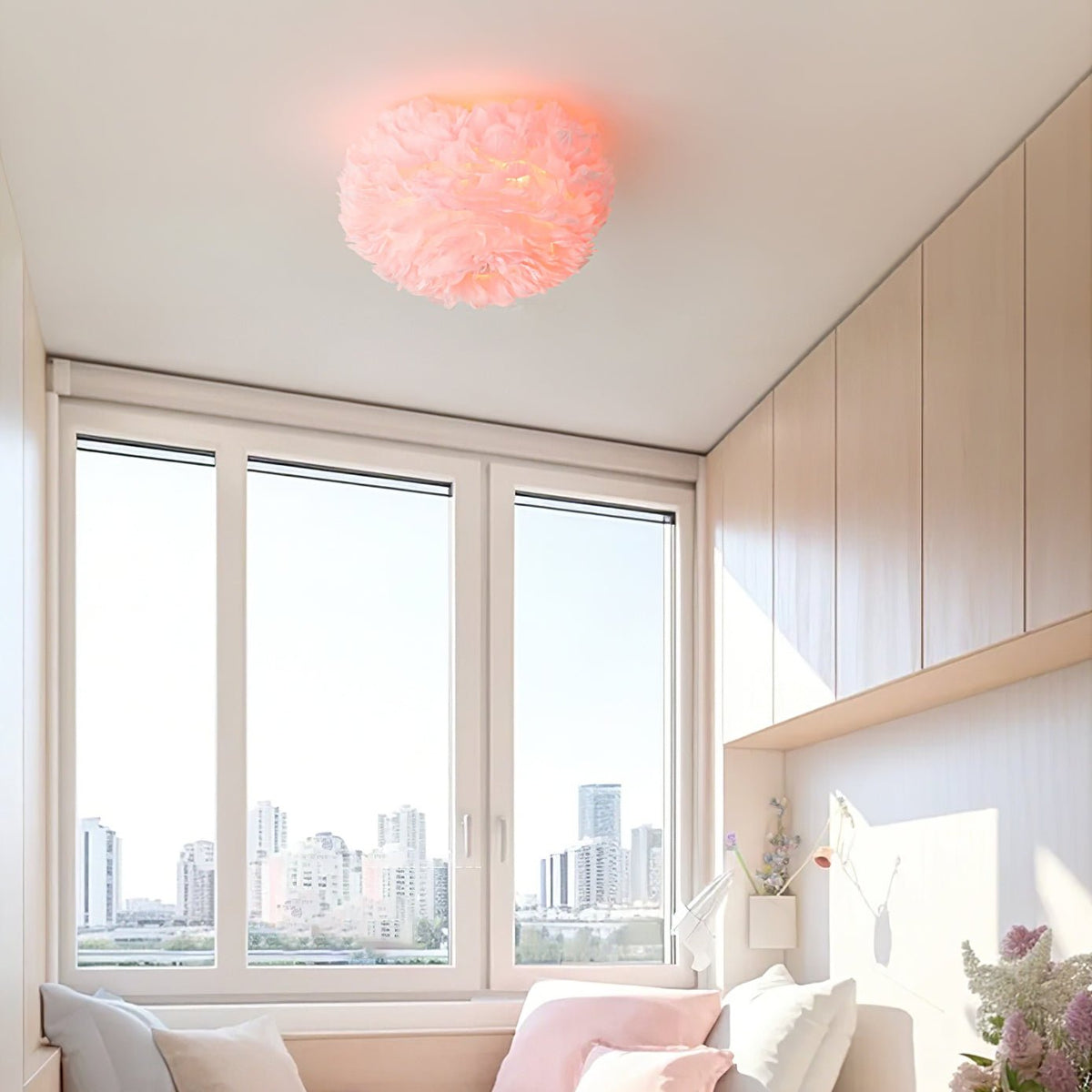 Pink feather ceiling light from Clérachic above a bright room with three tall windows, built-in cupboards and a pink window seat.