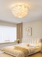 Lit white feather ceiling light from Clérachic over a bedroom with a tufted headboard, an ochre throw and a framed print.