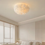 White feather ceiling light from Clérachic set against a cove-lit ceiling, with a pale ribbed wall and a bed edge below.