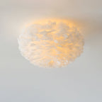 Close view of a white goose-feather ceiling light from Clérachic, lit warm so a soft halo spreads across the ceiling.