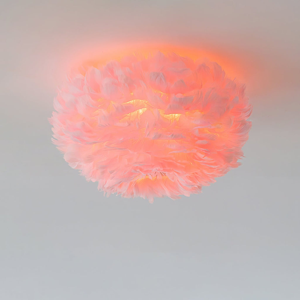 Pink feather ceiling light from Clérachic lit, with the feathers glowing coral against a pale grey ceiling.