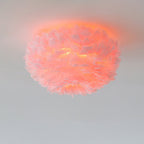 Pink feather ceiling light from Clérachic lit, with the feathers glowing coral against a pale grey ceiling.