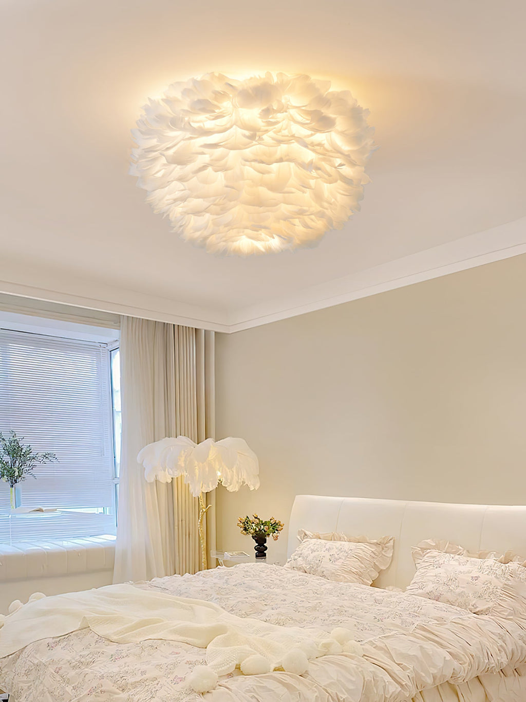 White feather ceiling light from Clérachic glowing above a cream bedroom with a feather floor lamp beside the bed.