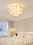 White feather ceiling light from Clérachic glowing above a cream bedroom with a feather floor lamp beside the bed.