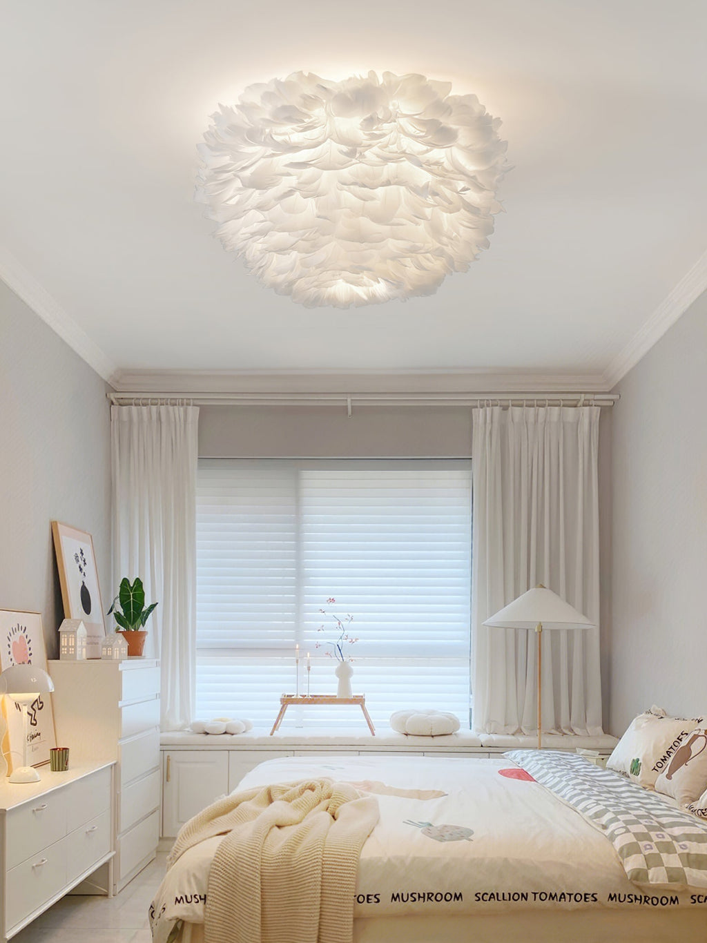 Clérachic white feather ceiling light seen from the doorway of a pale bedroom with a roller blind and a white chest of drawers.