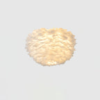 Lit white feather ceiling light from Clérachic with a warm glow showing through the layered feathers on a pale ceiling.