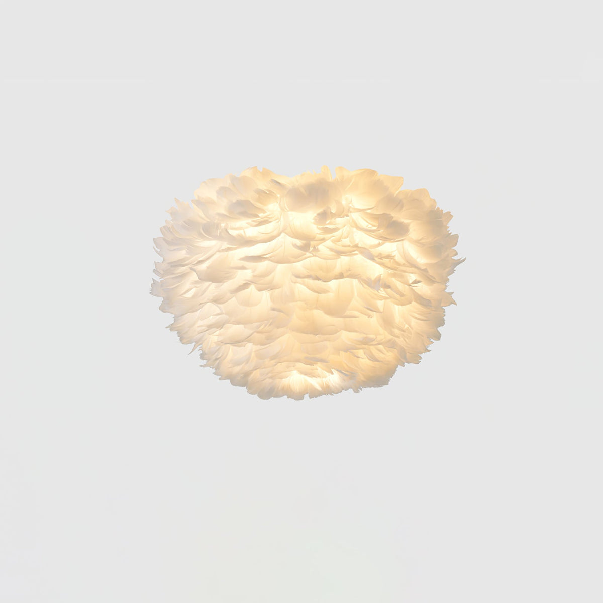 Lit white feather ceiling light from Clérachic with a warm glow showing through the layered feathers on a pale ceiling.