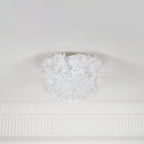 White goose-feather ceiling light from Clérachic, unlit, with feathers curling inward at the top where it meets a white ceiling.