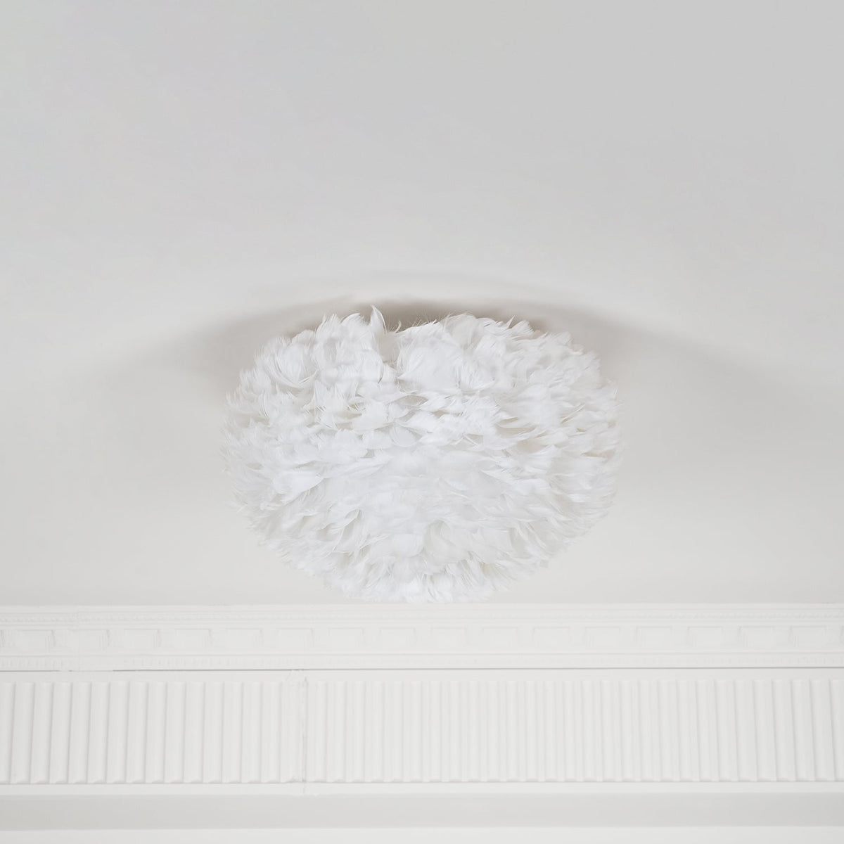 White goose-feather ceiling light from Clérachic, unlit, with feathers curling inward at the top where it meets a white ceiling.