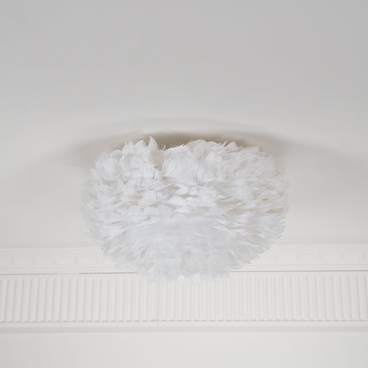 Unlit white feather ceiling light from Clérachic on a white ceiling above a ribbed plaster cornice, seen from the side.