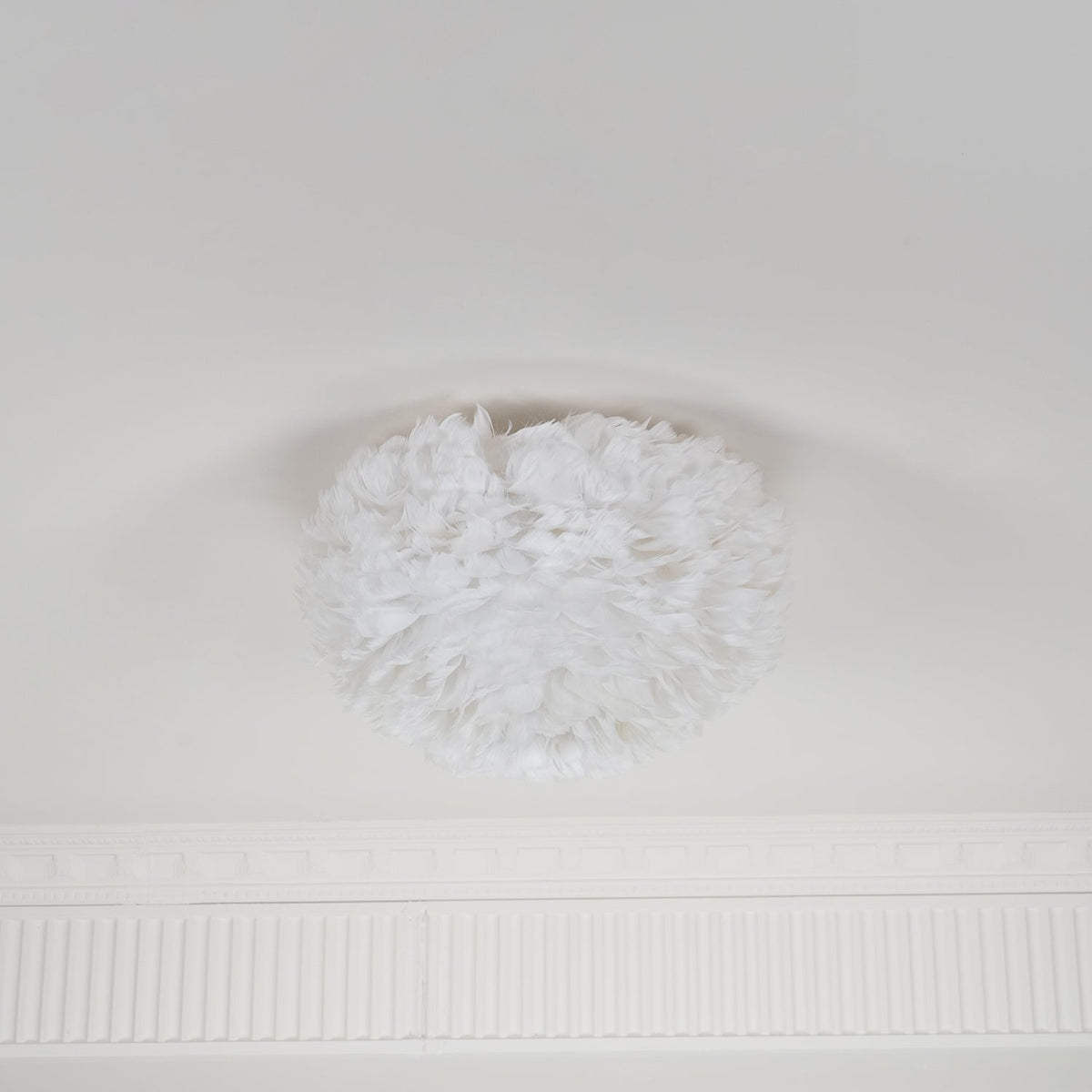 Small white feather ceiling light from Clérachic, unlit, on a pale ceiling with a decorative cornice below it.