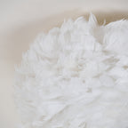 Close view of soft white goose feathers layered on the shade of this Clérachic ceiling light.