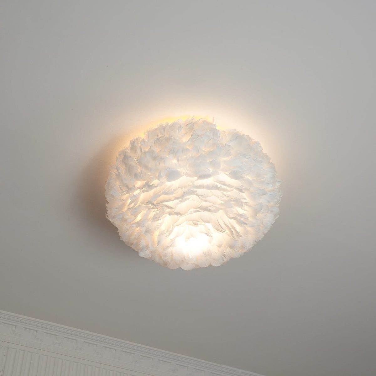 Lit white feather ceiling light from Clérachic with a warm glow on the ceiling and a bright patch under the shade.