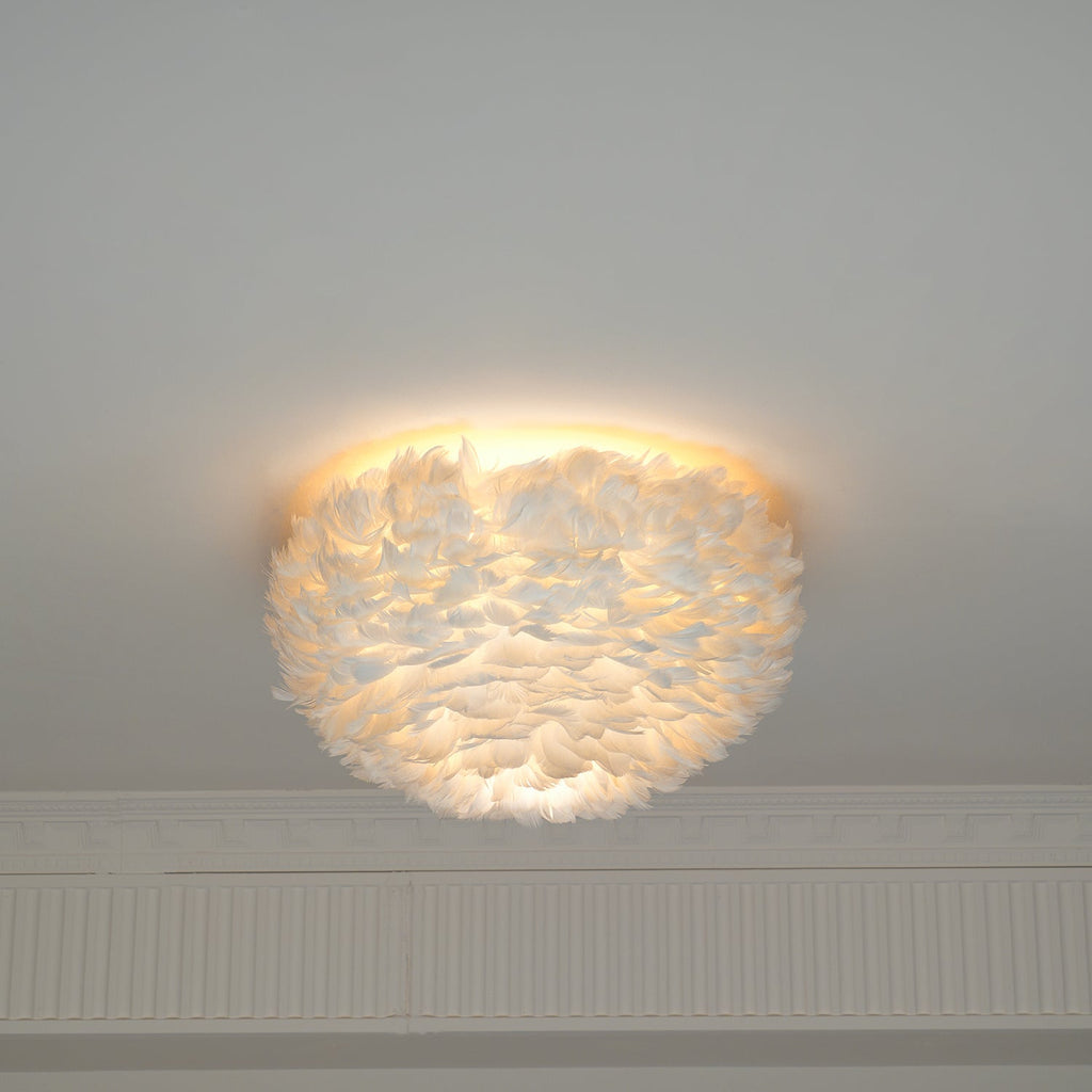 Lit white goose-feather ceiling light from Clérachic with a warm halo around its top edge, above a plaster cornice.