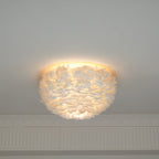 Lit white goose-feather ceiling light from Clérachic with a warm halo around its top edge, above a plaster cornice.