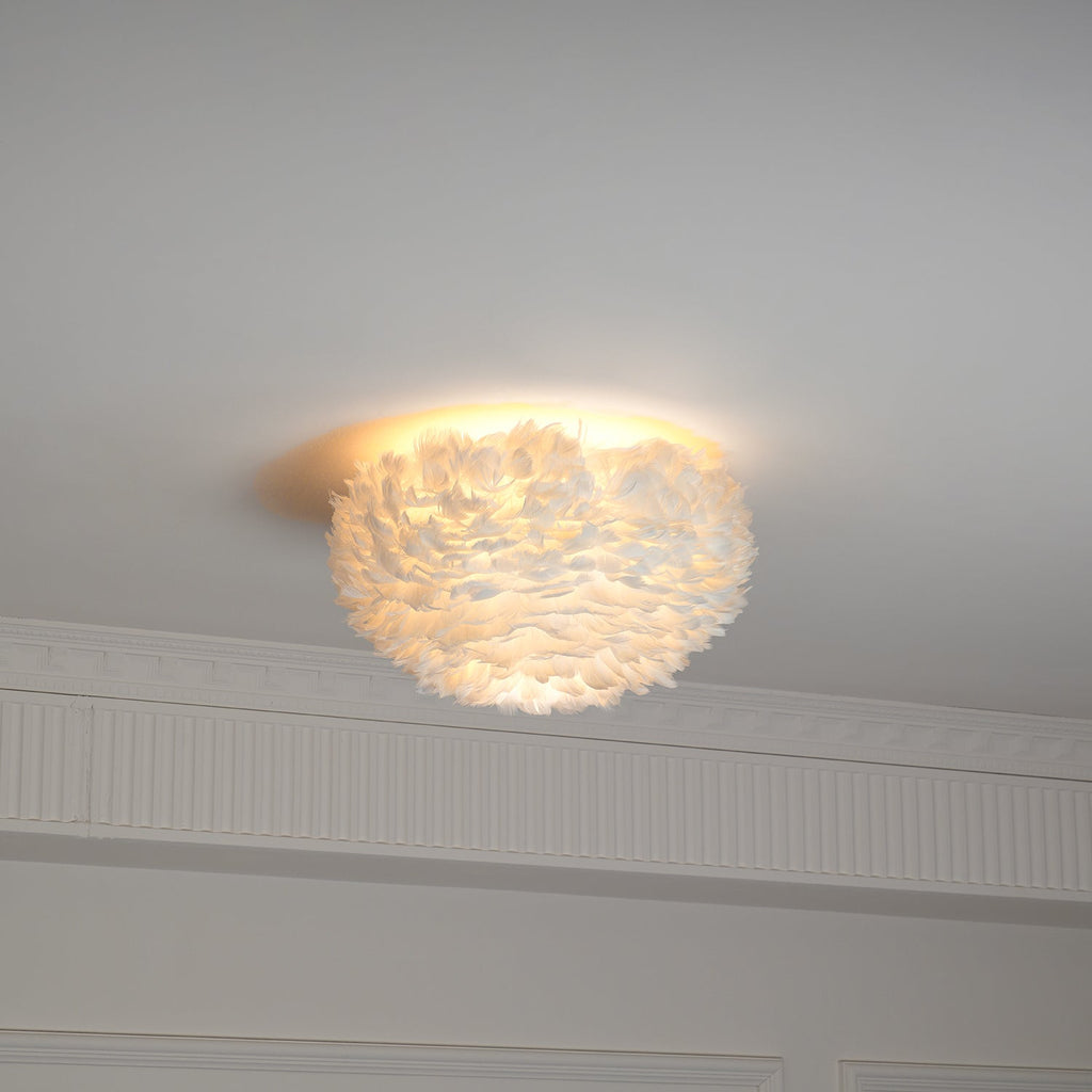 Feather ceiling light from Clérachic lit warm, seen from the side with a cornice and wall panelling beneath it.