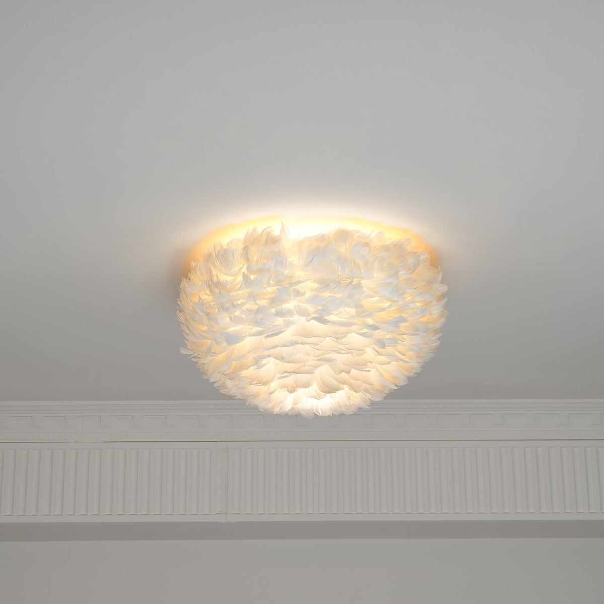 White feather ceiling light from Clérachic lit, with light glowing through the feathers and spilling up over the ceiling.