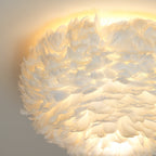 Close, lit view of white feathers on this Clérachic ceiling light, with warm light spreading across the ceiling above.