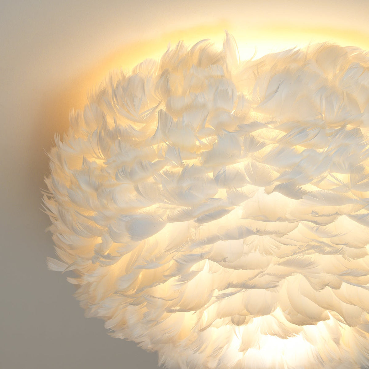 Close, lit view of white feathers on this Clérachic ceiling light, with warm light spreading across the ceiling above.