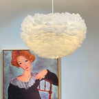Close under a Clérachic feather pendant lit warm from within, with a framed portrait painting in the background.