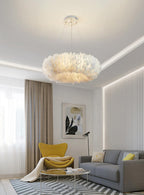 A Clérachic feather ring pendant hangs above a grey sofa, a yellow armchair and a round coffee table in a living room.