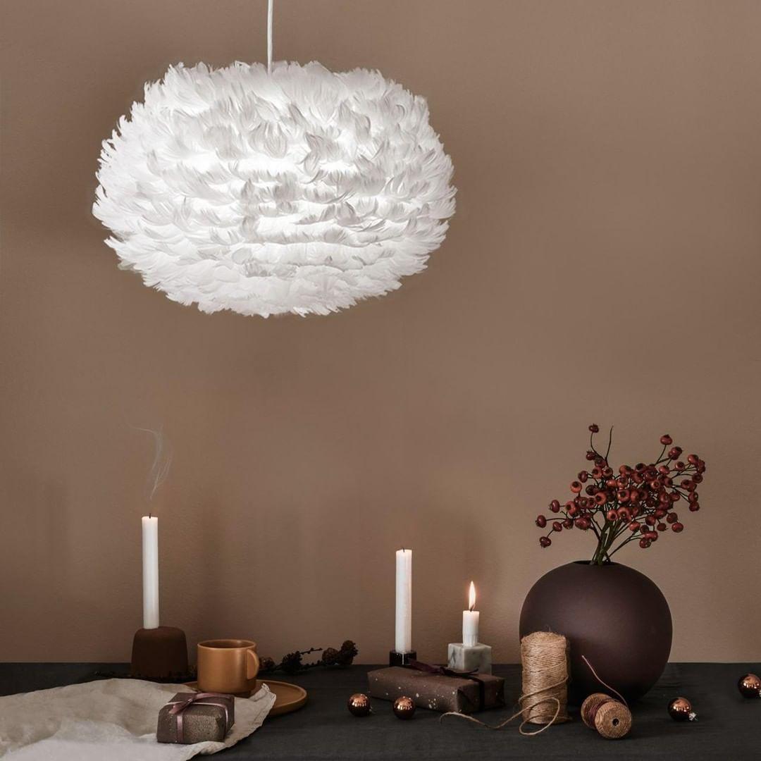 A white dome Clérachic feather pendant hangs against a brown wall, above candles, a dark vase and a few decor pieces.