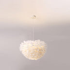 A round Clérachic feather pendant hangs on a single white cable against a soft grey-pink wall, lit warm from within.
