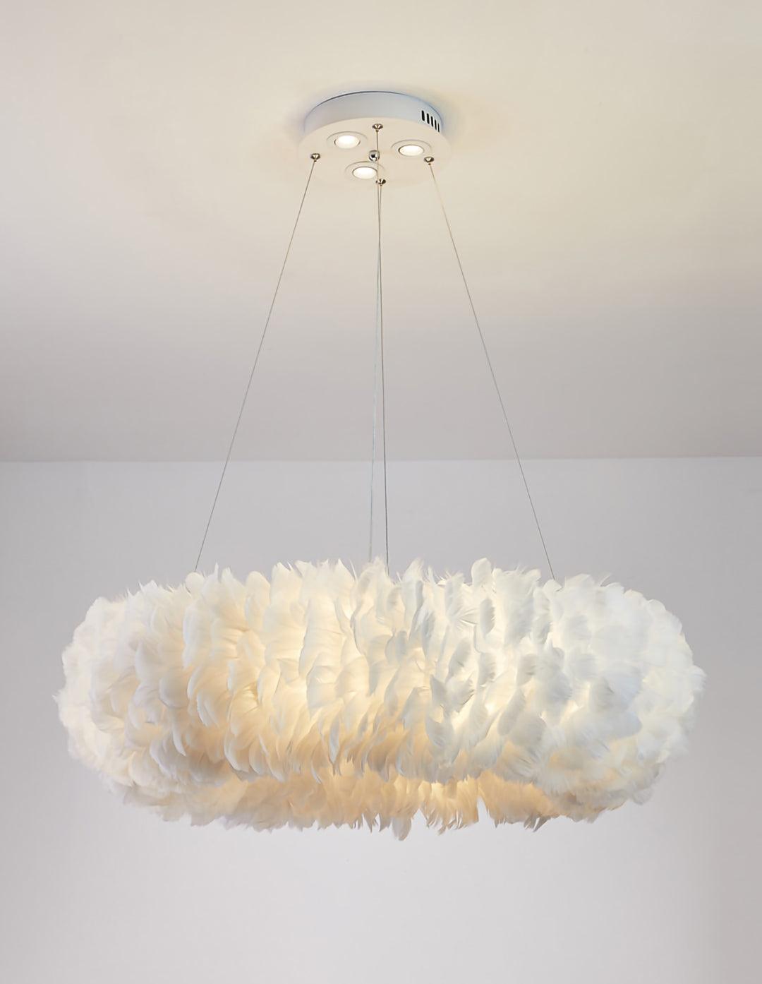 A Clérachic feather ring pendant lit warm white, hung on three cables in front of a plain pale wall.
