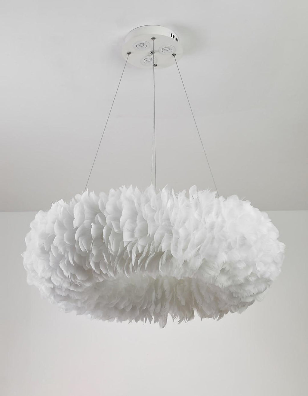 A Clérachic feather ring pendant unlit, showing the white feathers in layers, on three cables against a white wall.