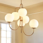 Clérachic gooseneck glass globe chandelier in gold, its six opal globes staggered above a sunlit room with a paned window.