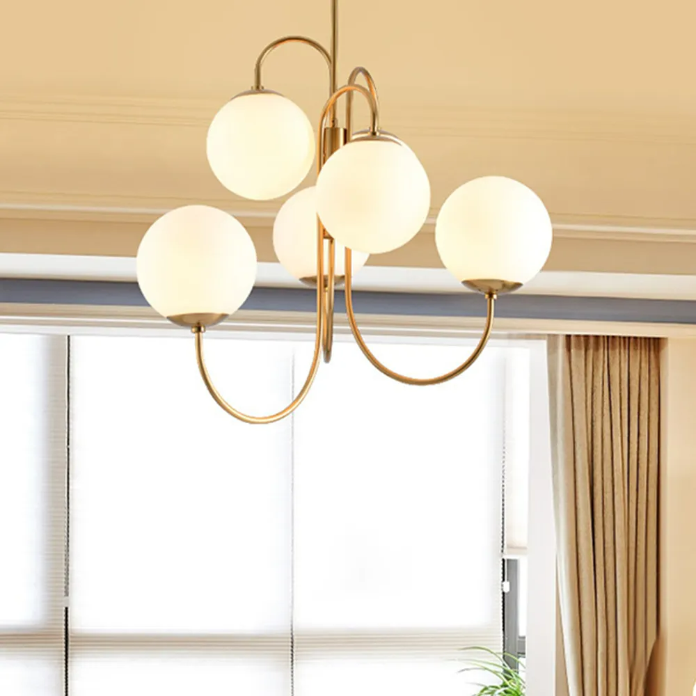 The Clérachic gold chandelier hangs close to a curtained window, its six lit globes casting a warm glow across the ceiling.