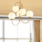 The Clérachic gold chandelier hangs close to a curtained window, its six lit globes casting a warm glow across the ceiling.