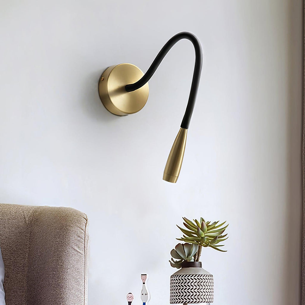 This Clérachic wall light with its gold backplate and a long curved black arm, shown above a plant in a patterned pot and a taupe armchair.