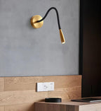 Gold Clérachic wall light on a grey wall above a wooden console and a dark panel, with its spot head angled down.