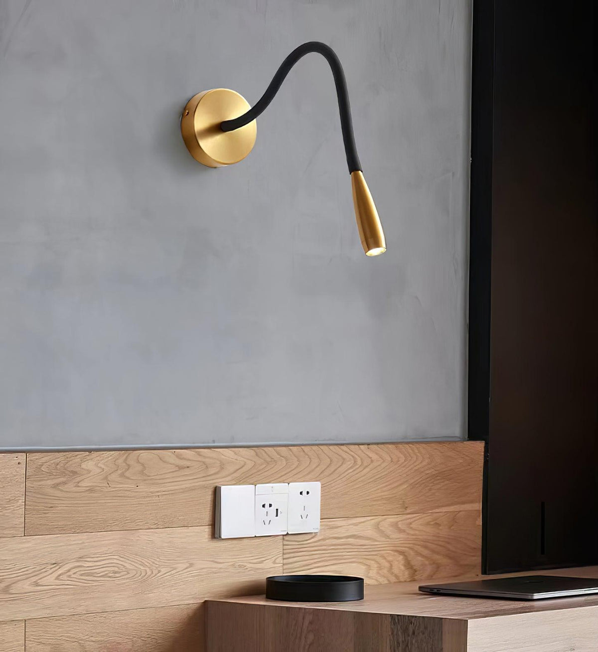 Gold Clérachic wall light on a grey wall above a wooden console and a dark panel, with its spot head angled down.