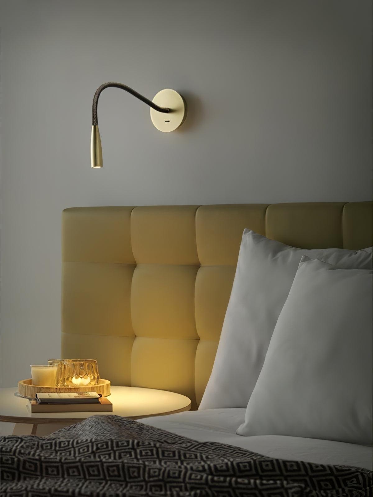A gold Clérachic reading wall light above a tufted headboard, with a round tray of candles on a small bedside table below.