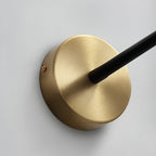 Close view of the round brushed gold backplate on this Clérachic wall light, with the black flexible arm leaving its centre and a fixing screw.