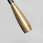 Close view of the tapered brushed gold spot head of this Clérachic wall light, ending in a small round lens on a pale grey ground.