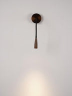 Lit Clérachic wall light in dark bronze with a straight, narrow black arm, throwing a soft pool of warm light down a pale wall.
