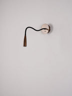 Clérachic wall light with a dark bronze spot head and a black arm bent in a gentle S-curve, on a grey-pink wall.
