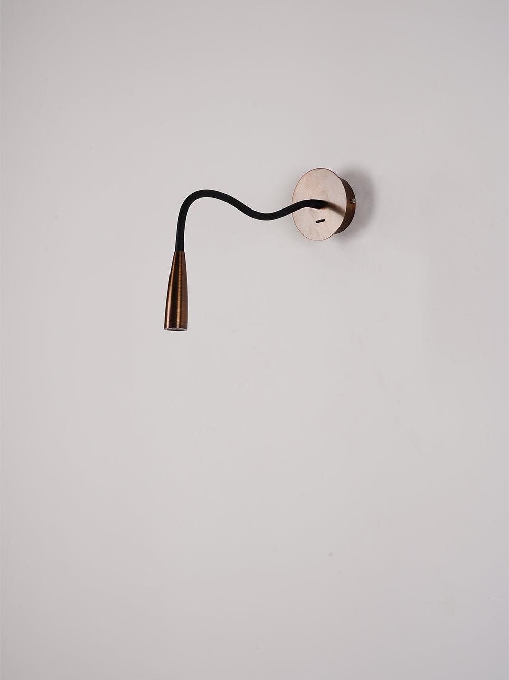 Clérachic wall light with a dark bronze spot head and a black arm bent in a gentle S-curve, on a grey-pink wall.