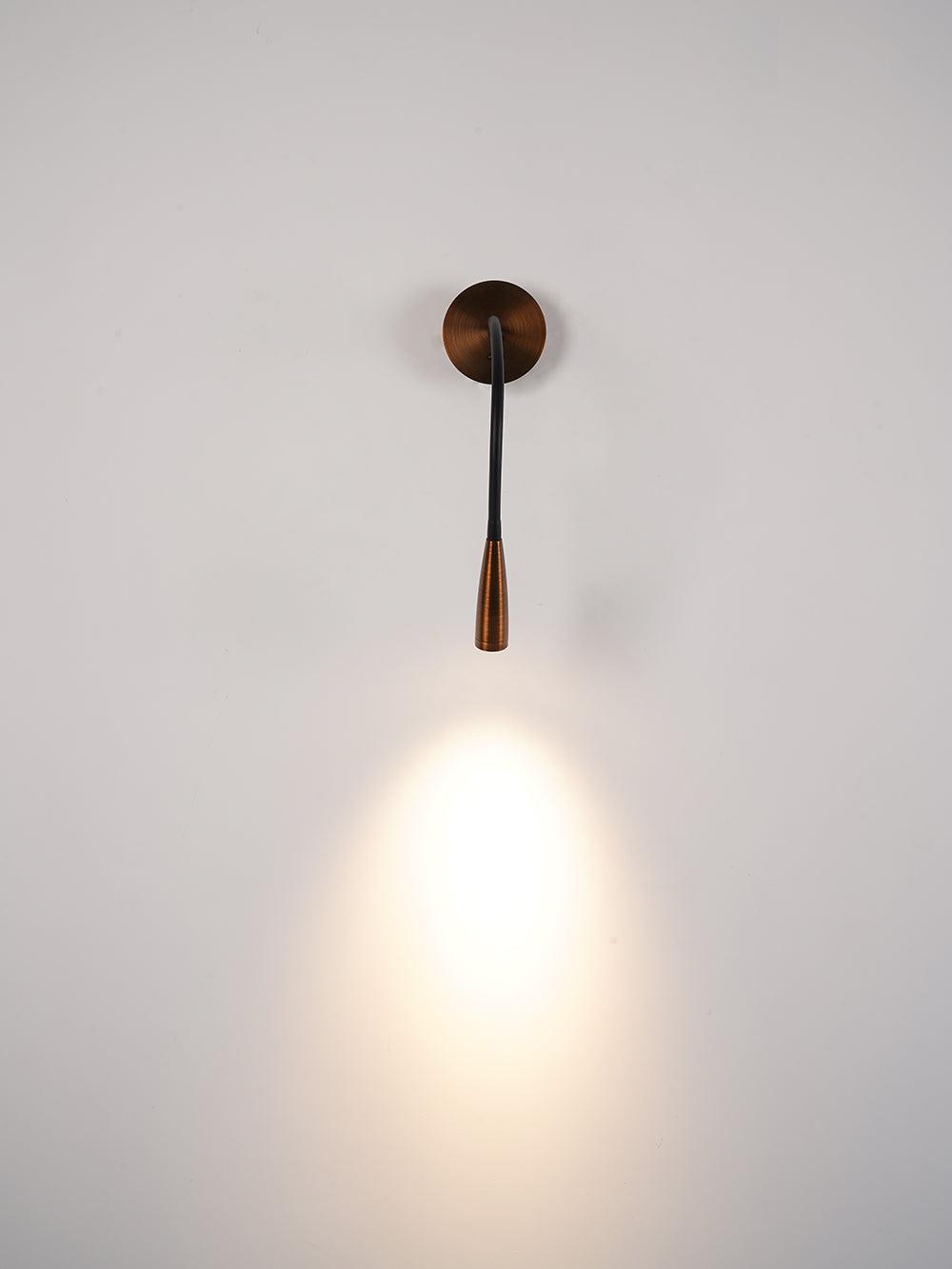 Dark bronze Clérachic wall light hanging straight down and casting a bright cone of warm light on a pale wall.