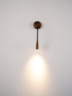 Dark bronze Clérachic wall light hanging straight down and casting a bright cone of warm light on a pale wall.